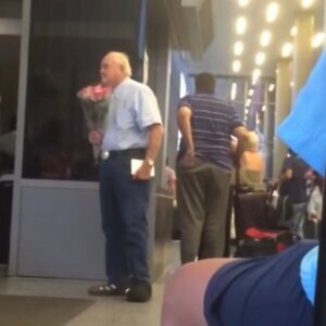 Elderly man secretly filmed waiting for his wife at airport with chocolate and flowers